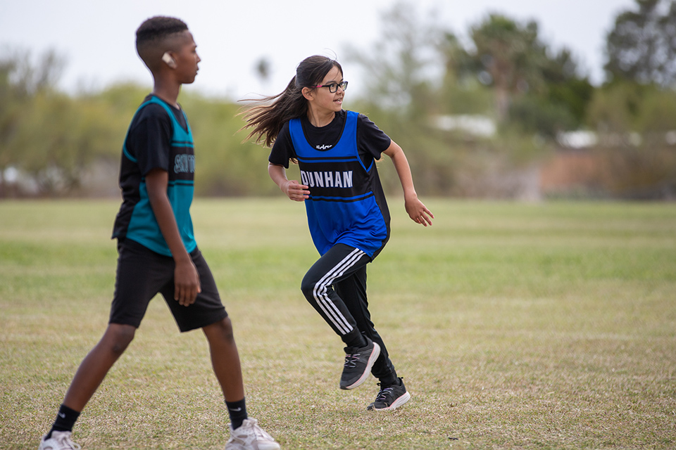 A girl in blue jersey runs past a boy in a teal jersey