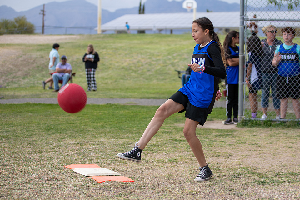A girl in a blue jersey kicks the red kickball
