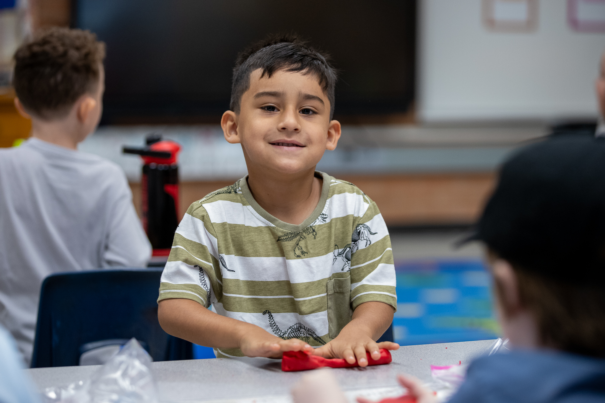 A little boy smiles while rolling out red playdoh 