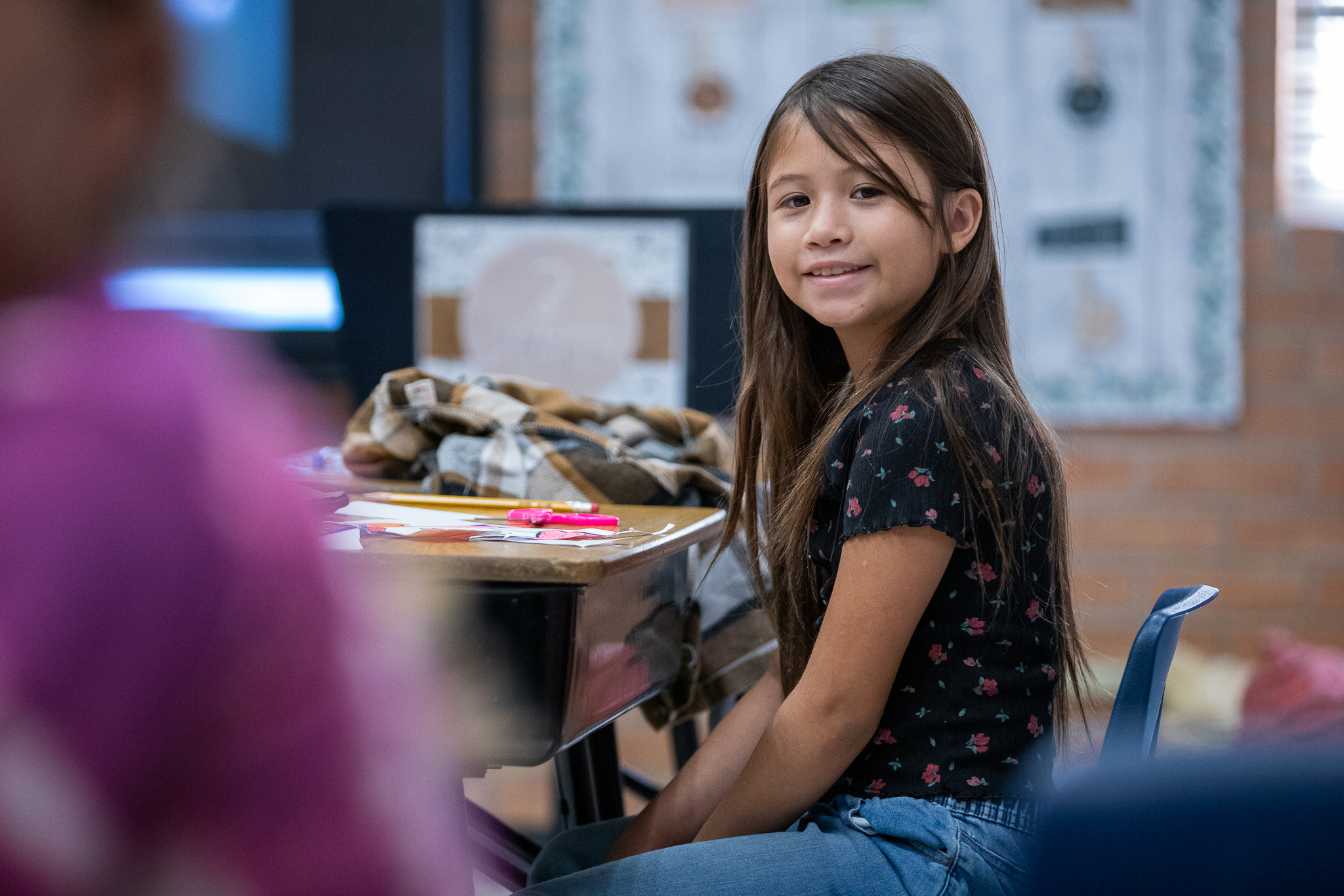 A little girl smiles at her desk on the second day of school