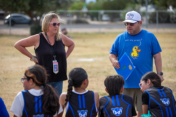 A woman and man coach a group of kids before the kickball game