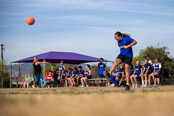 A girl kicks the kickball high in the air