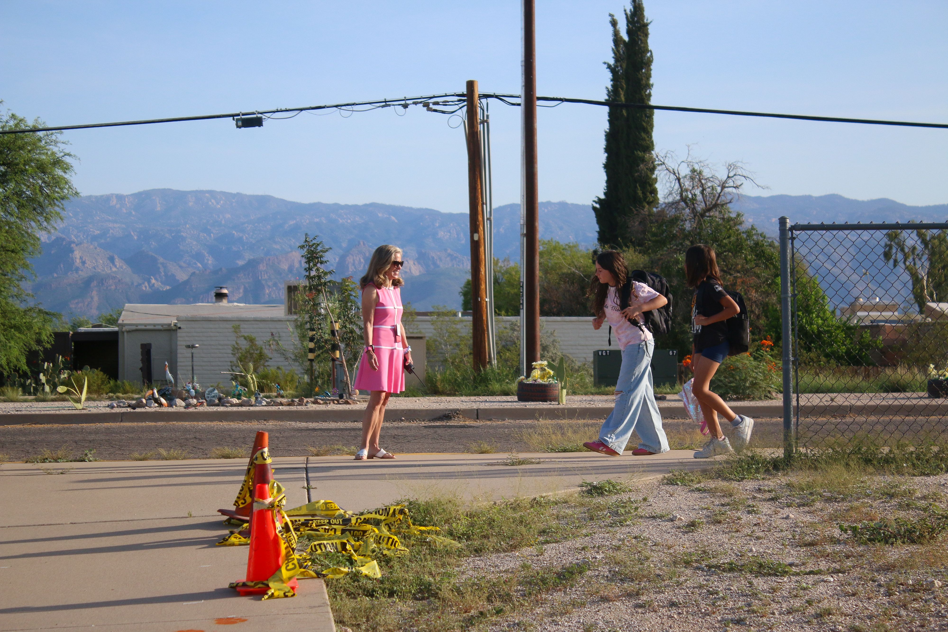 A woman in a pink dress stands by the curb to welcome students to school