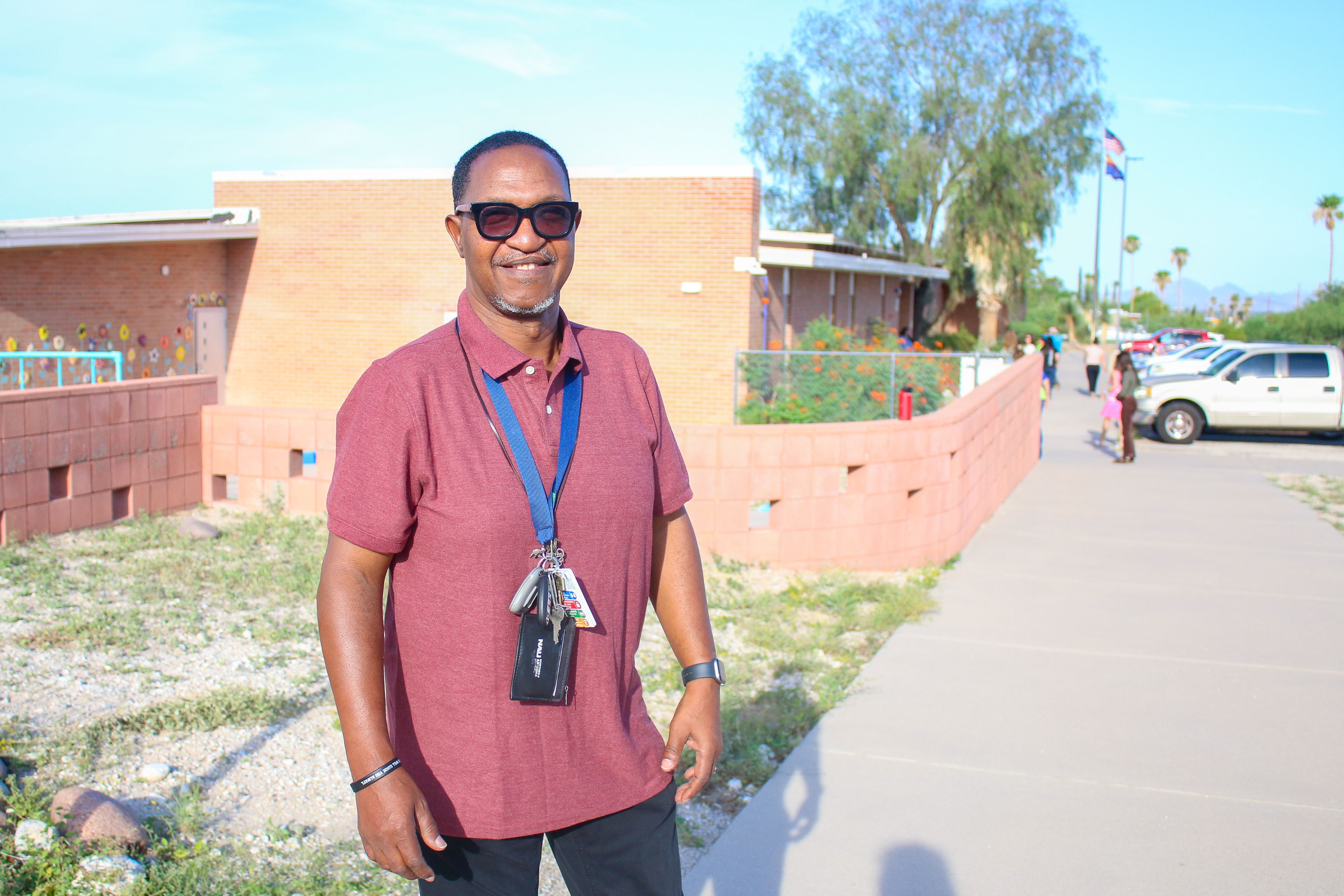 A man in a red shirt smiles outside the school